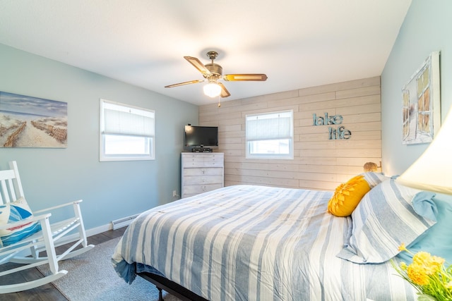 bedroom featuring a baseboard heating unit, ceiling fan, and wood walls