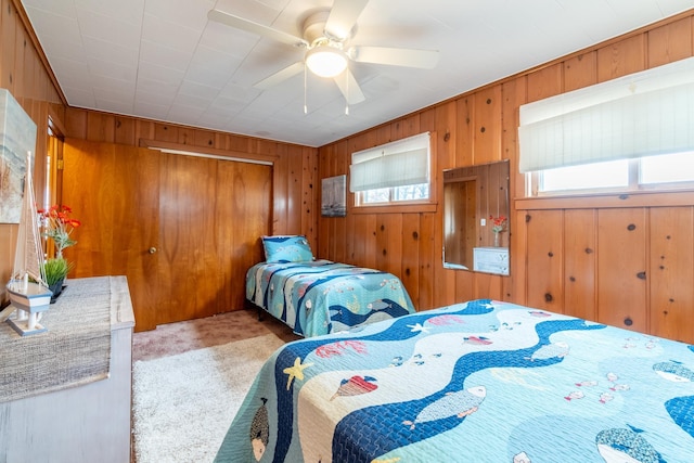 carpeted bedroom with a closet, ceiling fan, and wood walls