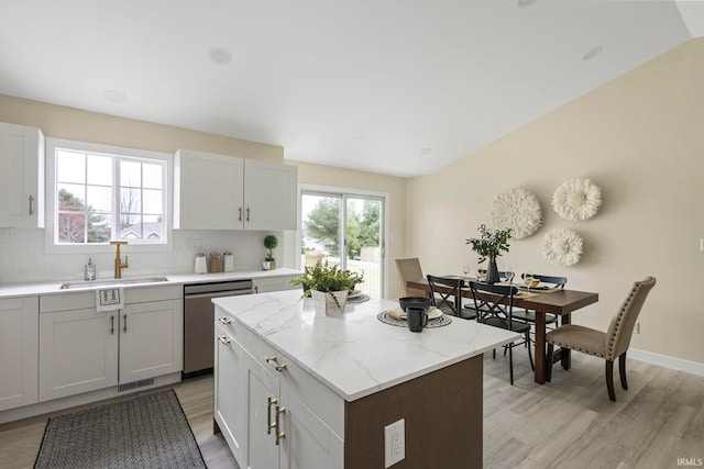 kitchen with sink, dishwasher, a center island, light stone counters, and tasteful backsplash