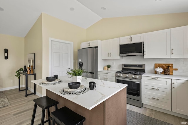 kitchen featuring stainless steel appliances, white cabinetry, a kitchen island, and vaulted ceiling