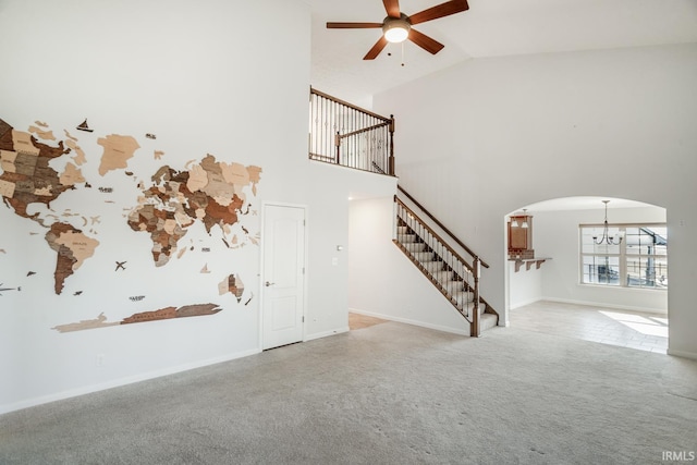 unfurnished living room with ceiling fan with notable chandelier, light colored carpet, and high vaulted ceiling