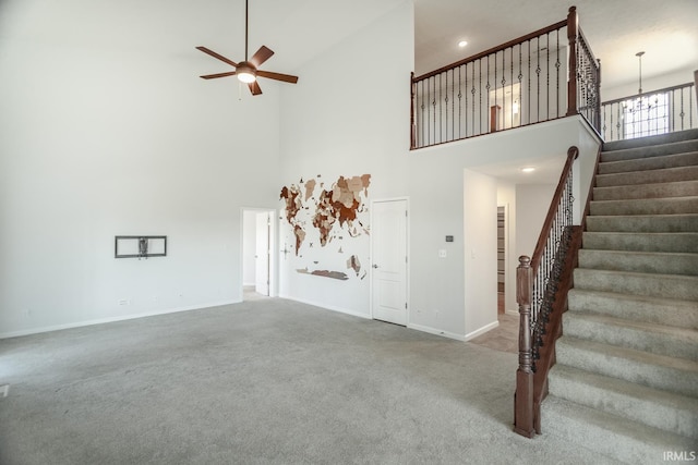 unfurnished living room featuring ceiling fan with notable chandelier, a high ceiling, and carpet