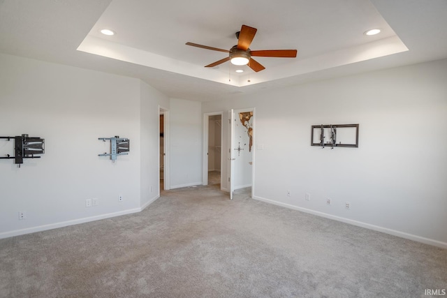 unfurnished room with light colored carpet, a raised ceiling, and ceiling fan