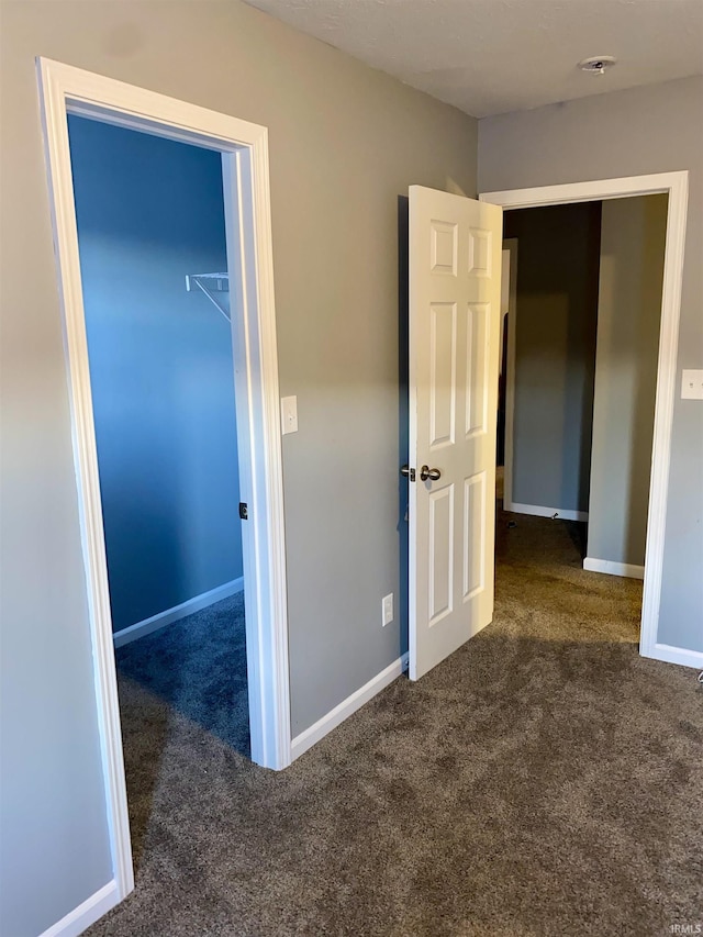 unfurnished bedroom with a spacious closet, dark carpet, and a closet