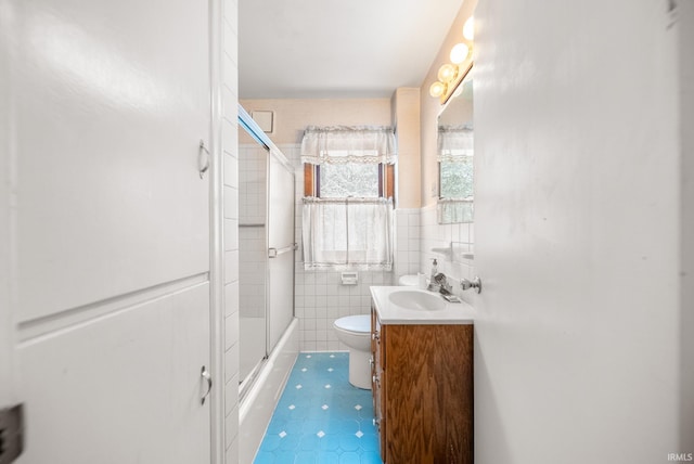 full bathroom featuring toilet, vanity, bath / shower combo with glass door, and tile walls