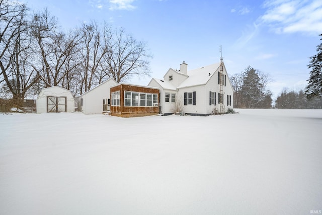 snow covered house with a storage shed and a sunroom