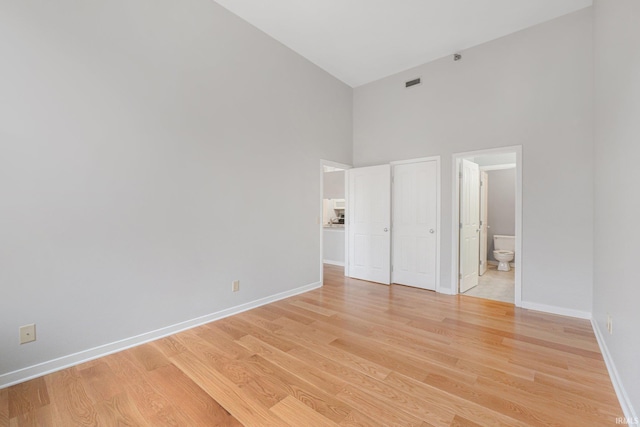 unfurnished bedroom featuring ensuite bathroom, a high ceiling, and light wood-type flooring