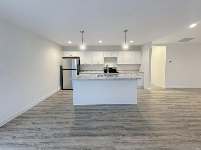 kitchen featuring sink, a center island with sink, white cabinets, and stainless steel refrigerator