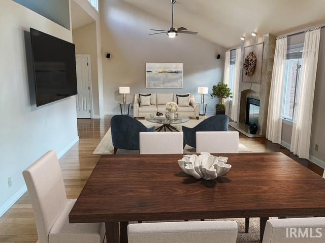 dining room featuring ceiling fan, a large fireplace, high vaulted ceiling, and light hardwood / wood-style floors