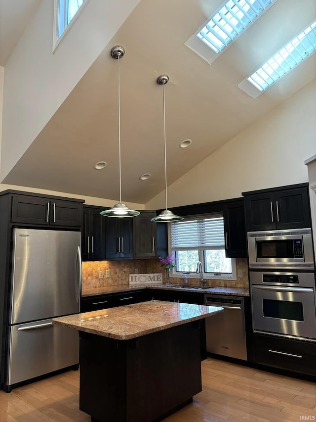 kitchen with a kitchen island, appliances with stainless steel finishes, decorative light fixtures, sink, and light stone counters