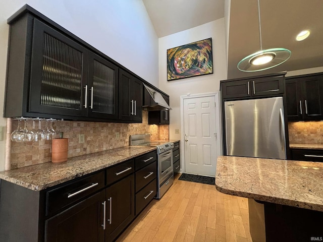 kitchen with appliances with stainless steel finishes, backsplash, hanging light fixtures, light hardwood / wood-style floors, and light stone countertops