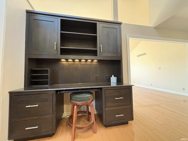 bar featuring dark brown cabinetry, built in desk, and light hardwood / wood-style flooring