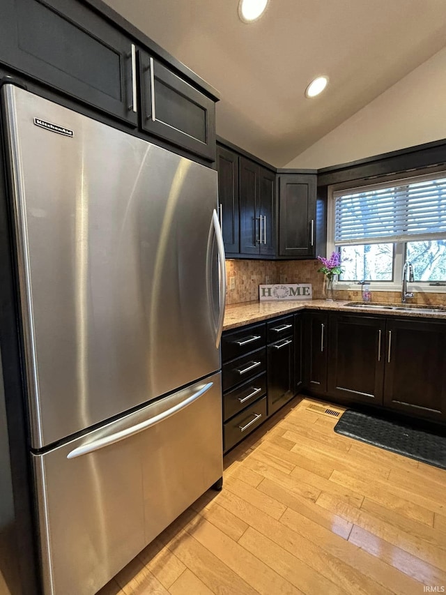 kitchen featuring vaulted ceiling, tasteful backsplash, sink, stainless steel fridge, and light wood-type flooring