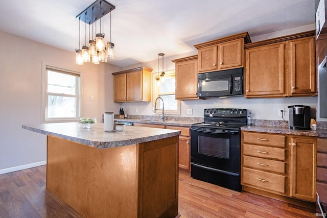 kitchen featuring sink, wood-type flooring, hanging light fixtures, a kitchen island, and black appliances