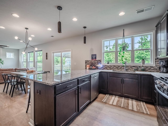 kitchen with decorative light fixtures, appliances with stainless steel finishes, kitchen peninsula, light stone countertops, and backsplash