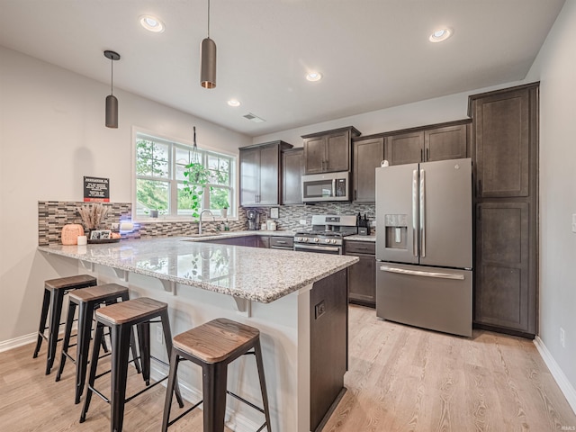 kitchen featuring pendant lighting, a kitchen bar, light stone counters, kitchen peninsula, and stainless steel appliances