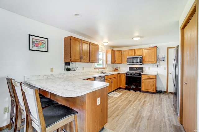 kitchen with sink, a breakfast bar, stainless steel appliances, light hardwood / wood-style floors, and kitchen peninsula