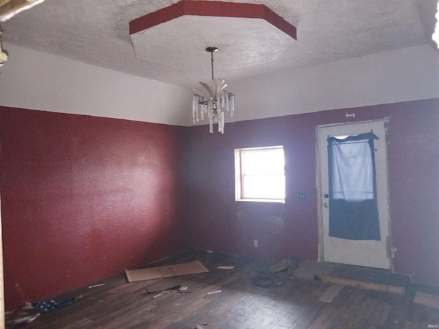 unfurnished dining area with an inviting chandelier, hardwood / wood-style floors, vaulted ceiling, and a textured ceiling