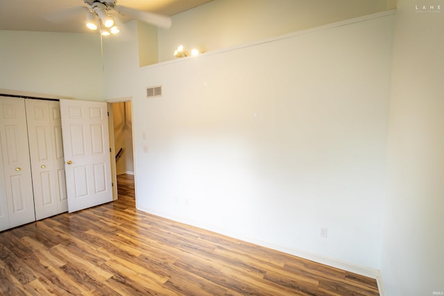 unfurnished bedroom featuring a towering ceiling, wood-type flooring, a closet, and ceiling fan