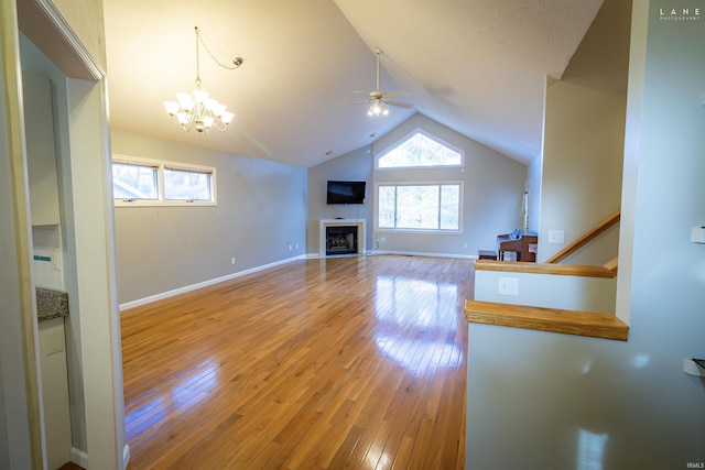 unfurnished living room with vaulted ceiling, a healthy amount of sunlight, ceiling fan with notable chandelier, and hardwood / wood-style floors