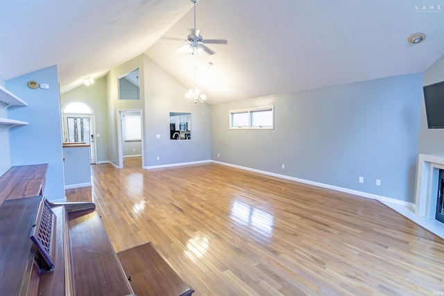 unfurnished living room with high vaulted ceiling, ceiling fan with notable chandelier, and light wood-type flooring