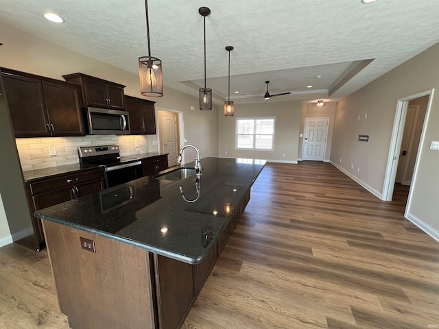 kitchen with pendant lighting, sink, a kitchen island with sink, stainless steel appliances, and a raised ceiling