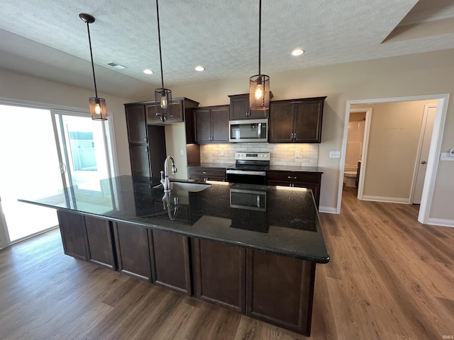 kitchen with dark brown cabinetry, sink, hanging light fixtures, an island with sink, and stainless steel appliances