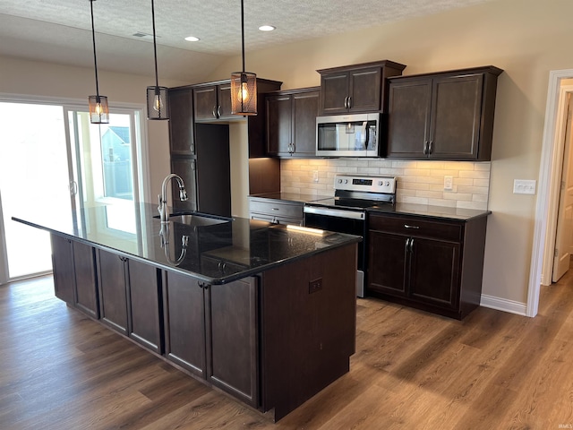 kitchen featuring pendant lighting, appliances with stainless steel finishes, sink, and a kitchen island with sink