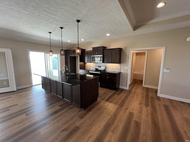 kitchen with sink, dark wood-type flooring, stainless steel appliances, tasteful backsplash, and an island with sink