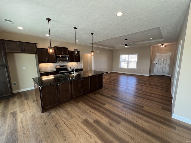 kitchen with dark brown cabinetry, stainless steel appliances, a raised ceiling, and a center island with sink