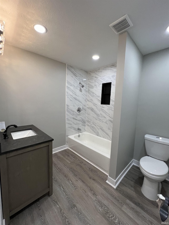 full bathroom featuring vanity, hardwood / wood-style floors, tiled shower / bath combo, and toilet