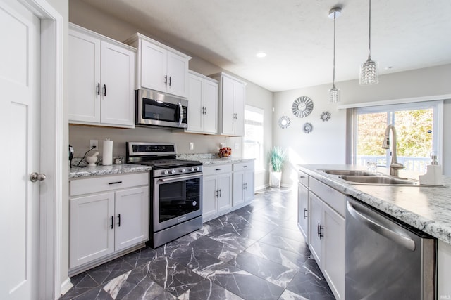 kitchen featuring decorative light fixtures, sink, white cabinets, stainless steel appliances, and light stone countertops