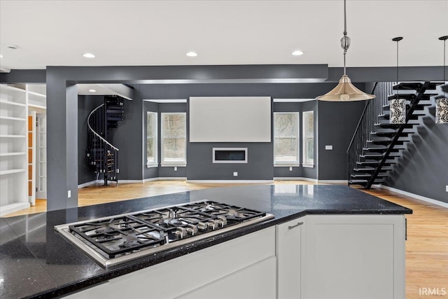 kitchen featuring stainless steel gas cooktop, white cabinetry, hanging light fixtures, dark stone countertops, and a wealth of natural light