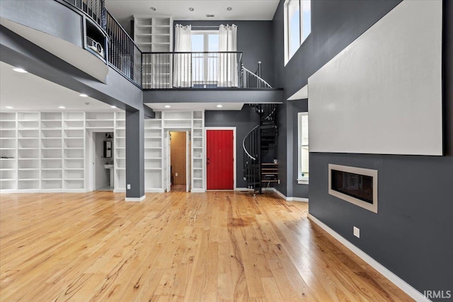 unfurnished living room with a towering ceiling, wood-type flooring, and built in features