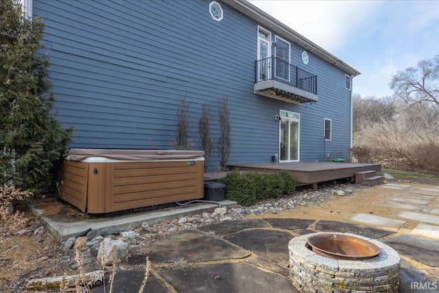 back of house featuring a balcony, an outdoor fire pit, a hot tub, and a deck