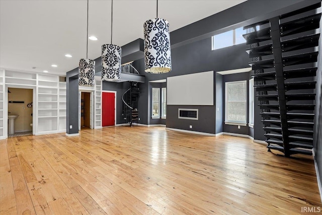 unfurnished living room with a towering ceiling, hardwood / wood-style floors, built in features, and a wealth of natural light