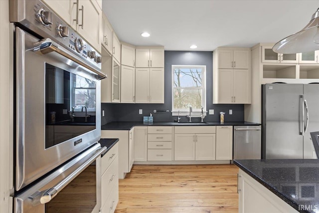 kitchen featuring stainless steel appliances, sink, dark stone counters, and light hardwood / wood-style flooring