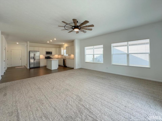 unfurnished living room with ceiling fan and dark colored carpet