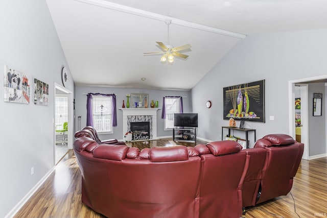 living room with vaulted ceiling, ceiling fan, a stone fireplace, and hardwood / wood-style floors