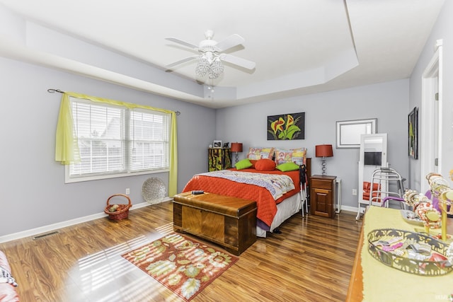 bedroom featuring a tray ceiling, wood-type flooring, and ceiling fan