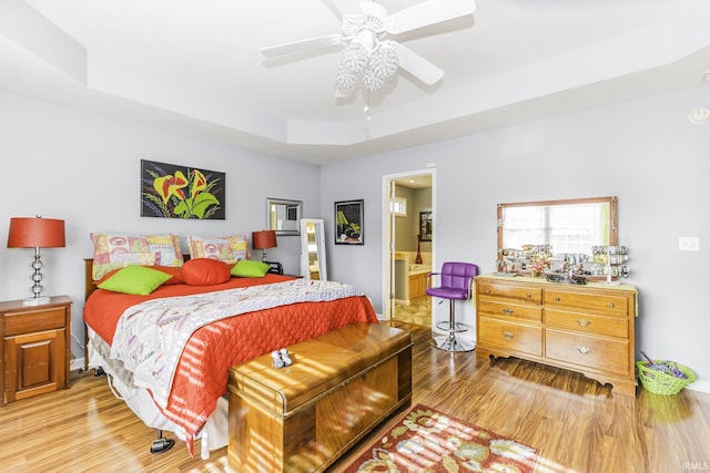 bedroom with ceiling fan, light hardwood / wood-style flooring, ensuite bath, and a tray ceiling