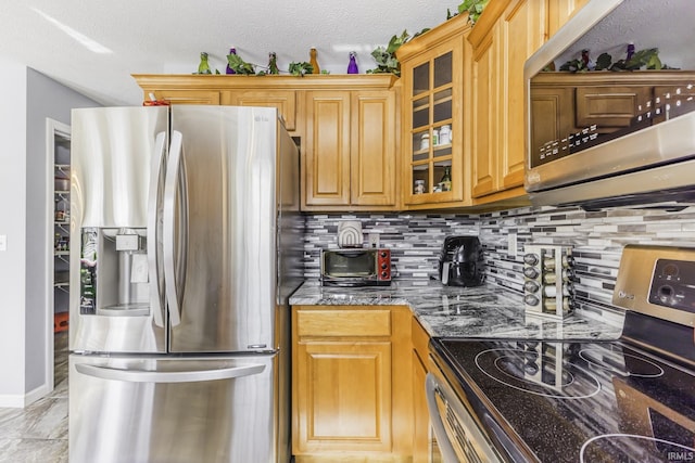 kitchen featuring tasteful backsplash, appliances with stainless steel finishes, a textured ceiling, and dark stone counters