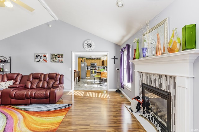 living room with hardwood / wood-style flooring, a tiled fireplace, vaulted ceiling, and ceiling fan