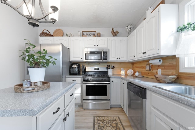 kitchen featuring appliances with stainless steel finishes, white cabinetry, a chandelier, a textured ceiling, and light hardwood / wood-style flooring