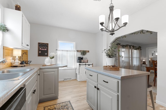 kitchen featuring sink, gray cabinetry, hanging light fixtures, stainless steel dishwasher, and light wood-type flooring