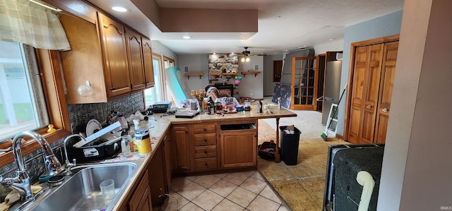 kitchen featuring sink, tasteful backsplash, light tile patterned floors, ceiling fan, and a fireplace