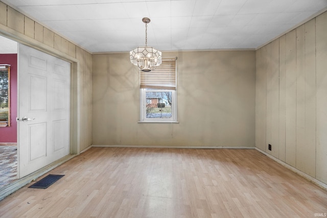 empty room featuring an inviting chandelier, light wood-type flooring, and wood walls