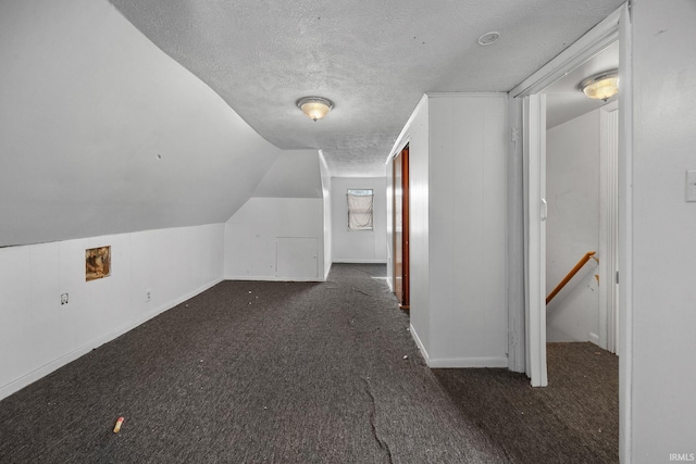 additional living space featuring lofted ceiling, dark carpet, and a textured ceiling