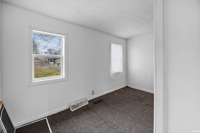 unfurnished room with a wealth of natural light, a textured ceiling, and dark colored carpet