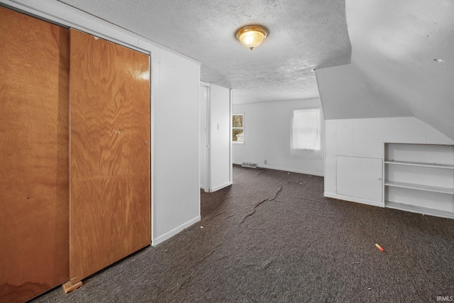 additional living space with lofted ceiling, dark carpet, and a textured ceiling